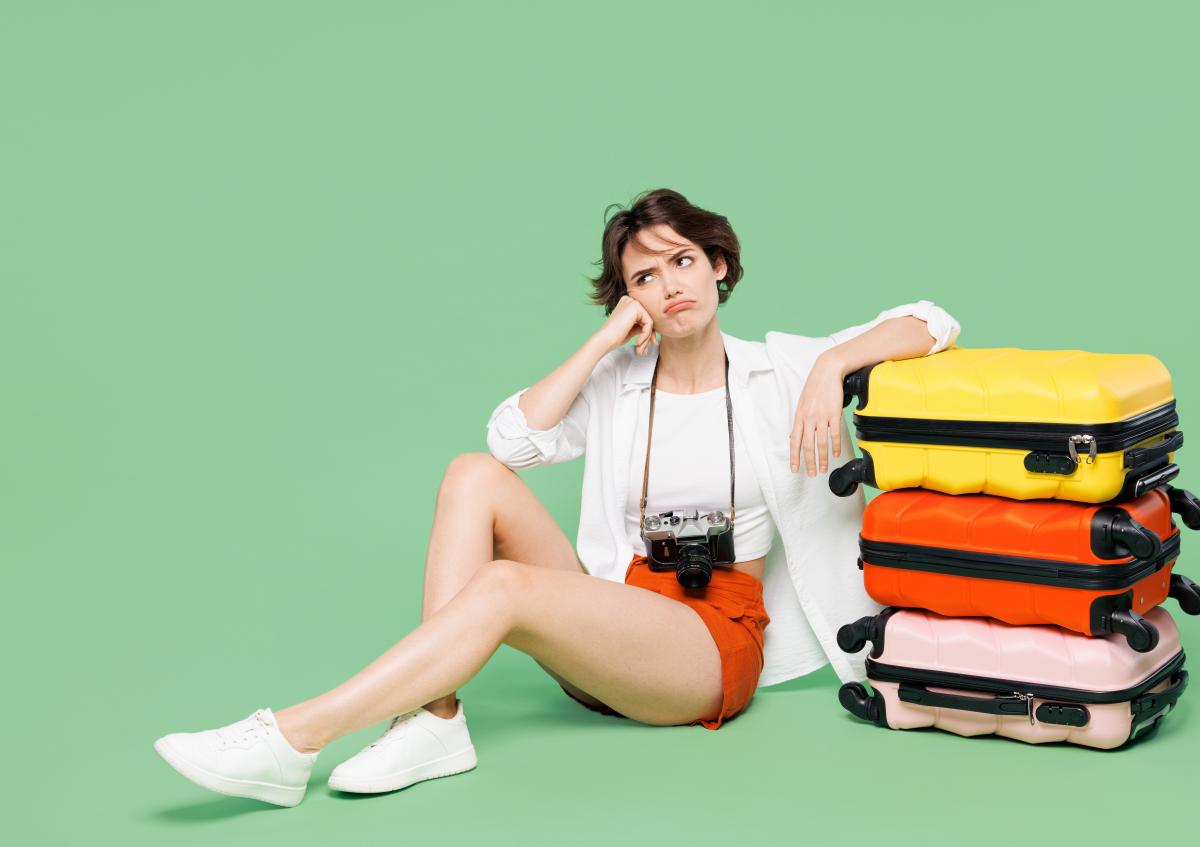 Vrouw zit op de grond naast koffers, zichtbaar teleurgesteld en gefrustreerd
