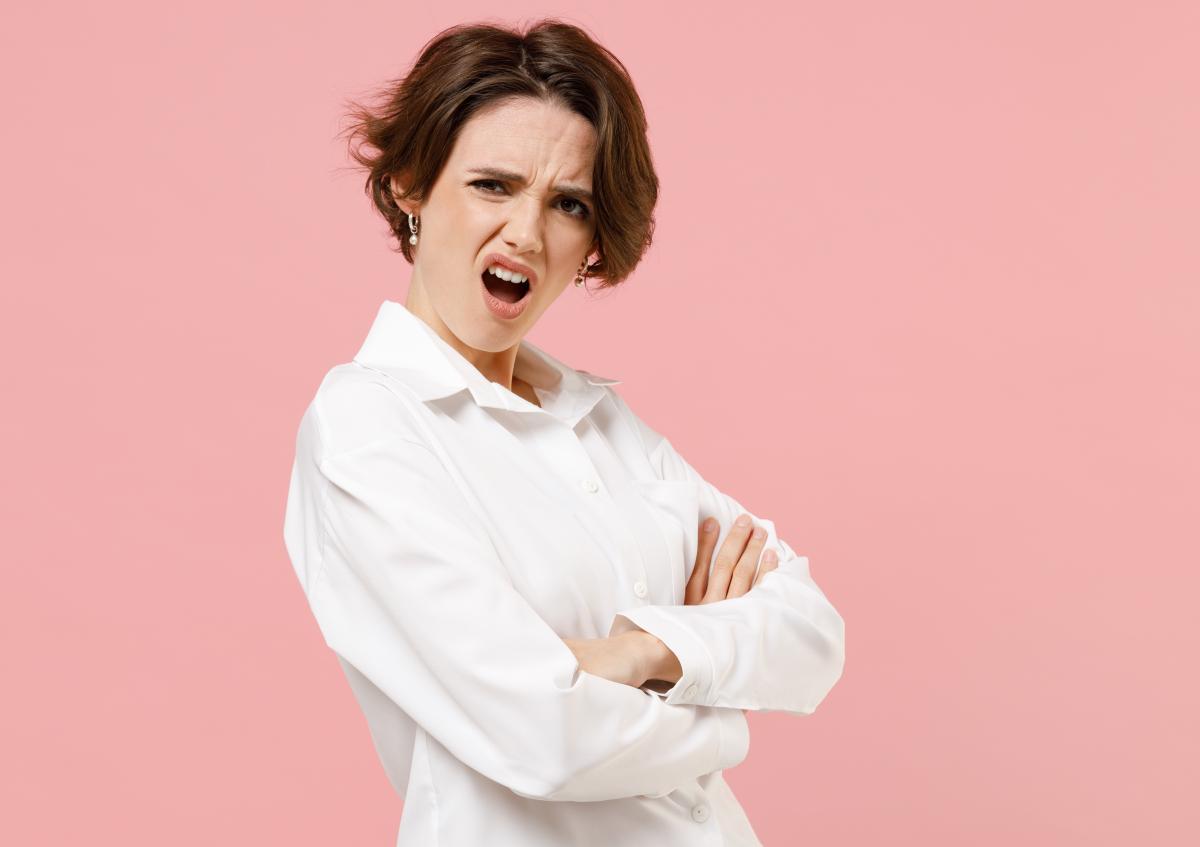 Vrouw kijkt met opgetrokken wenkbrauwen en open mond verbaasd of sceptisch naar iets buiten beeld. Ze staat met gekruiste armen.