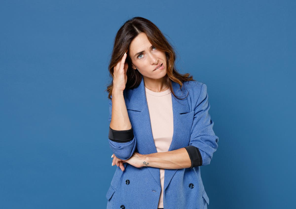 A woman with a thoughtful and slightly puzzled expression, resting one hand on her temple while biting her lip.