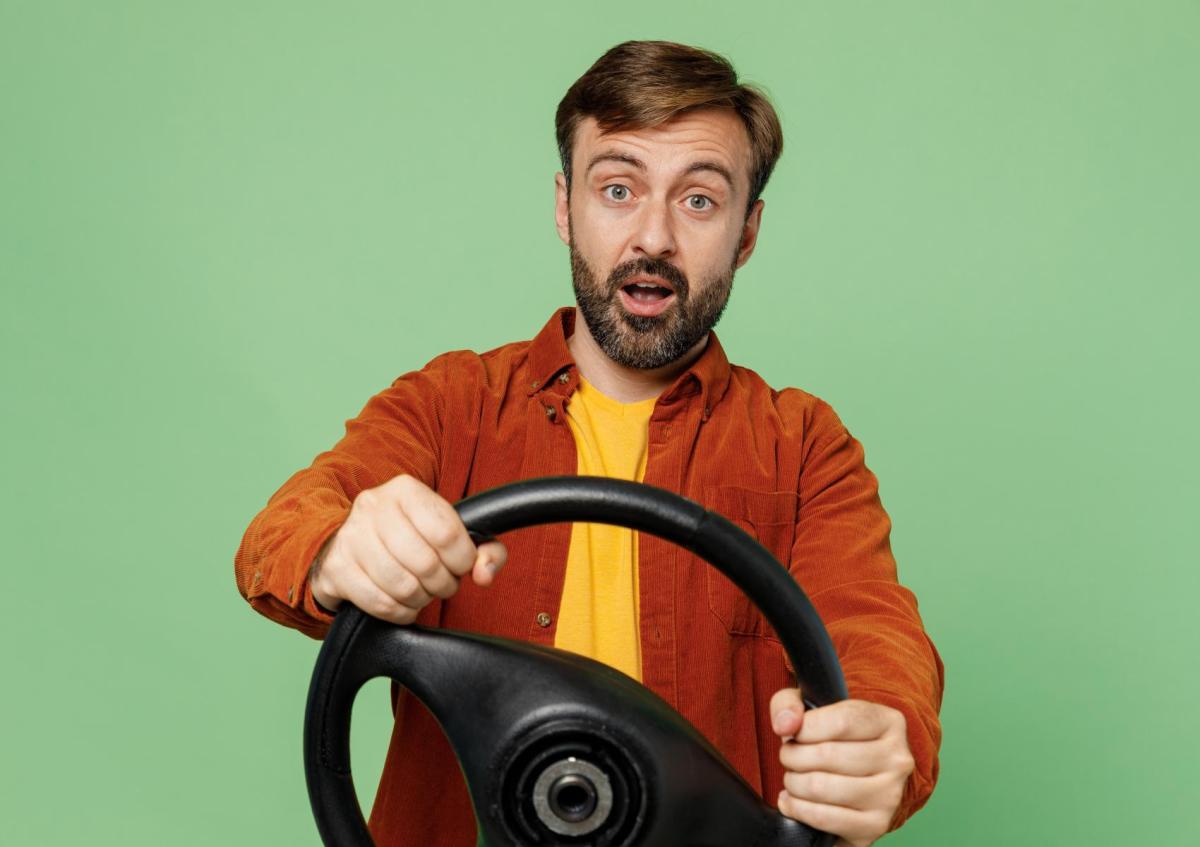 Een verraste man houdt het stuur met beide handen vast. Hij kijkt recht vooruit met grote ogen en een open mond.