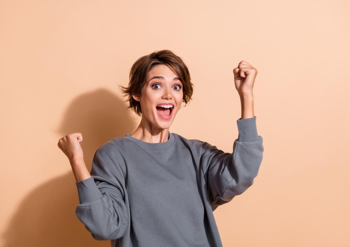 A young woman raising her fists excitedly with a wide open smile, expressing joy or celebration.