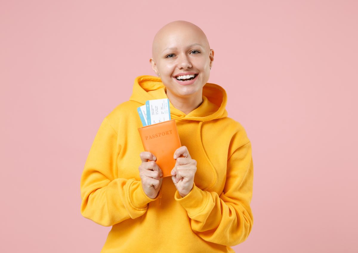 A joyful woman with a shaved head is smiling widely, holding a passport with visible boarding passes