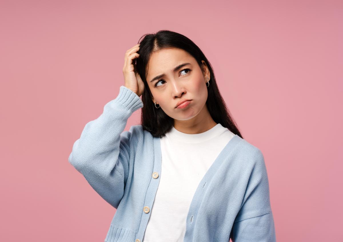 A young woman scratching her head with a puzzled or thoughtful expression, looking slightly to the side.