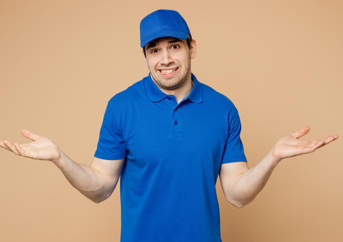 A delivery man with a slightly doubtful or uneasy expression shrugs his shoulders and spreads his hands outward as if he doesn’t know or isn’t sure about something.