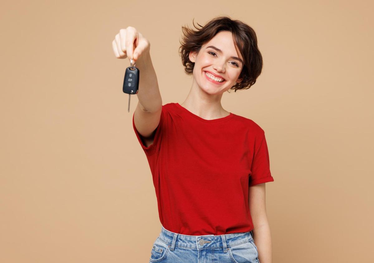 A cheerful young woman holds out a car key towards the camera, smiling broadly.