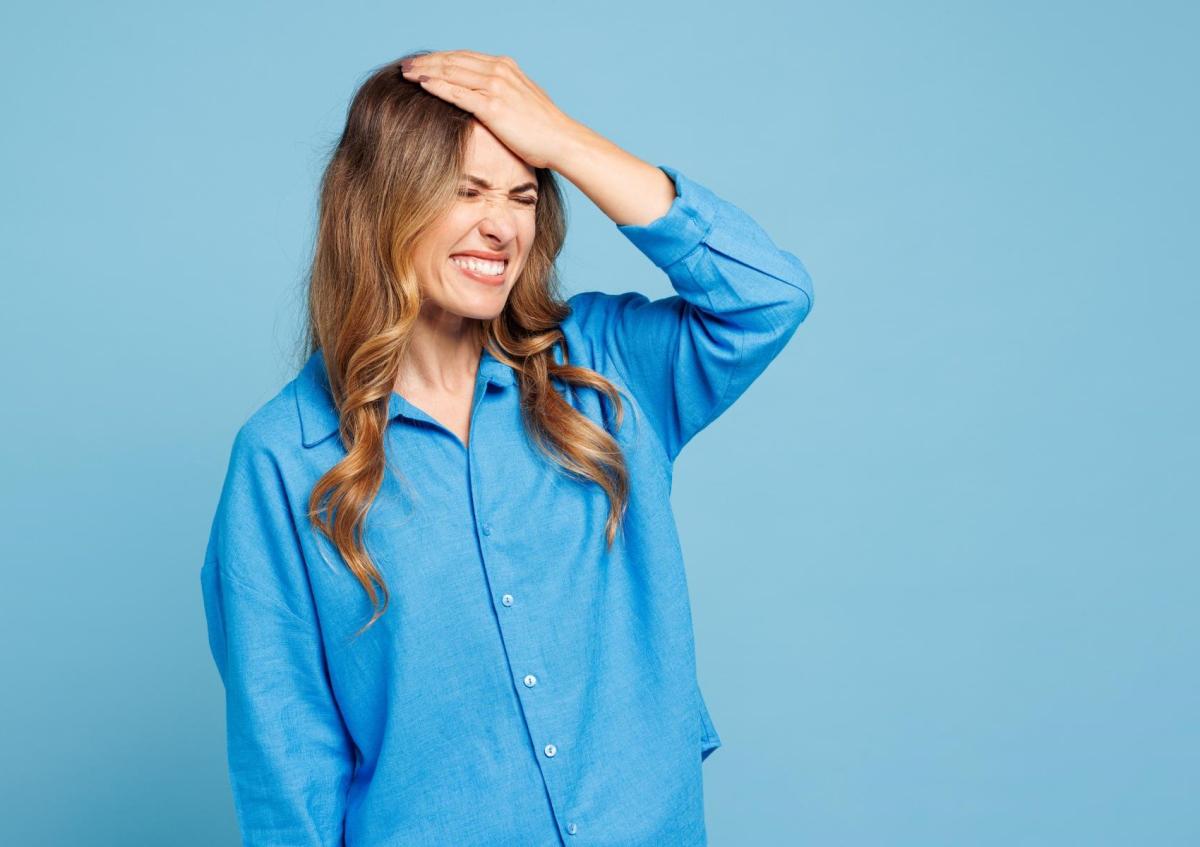 Een vrouw drukt haar hand tegen haar voorhoofd, sluit haar ogen stevig en trekt een grimas, waarmee ze frustratie uitdrukt.