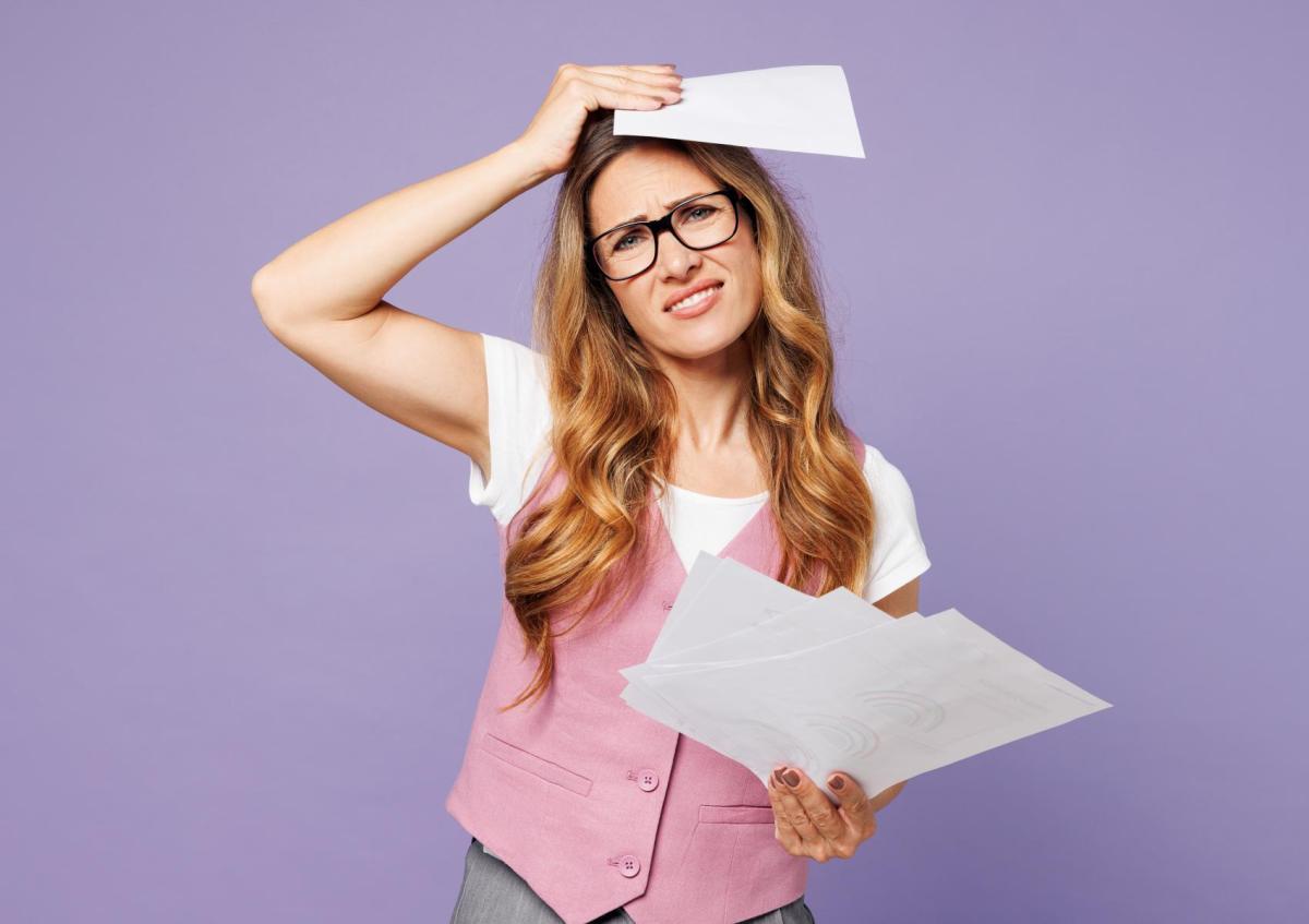 Vrouw kijkt boos en gefrustreerd met open mond. Ze houdt een stapel papieren in beide handen omhoog.