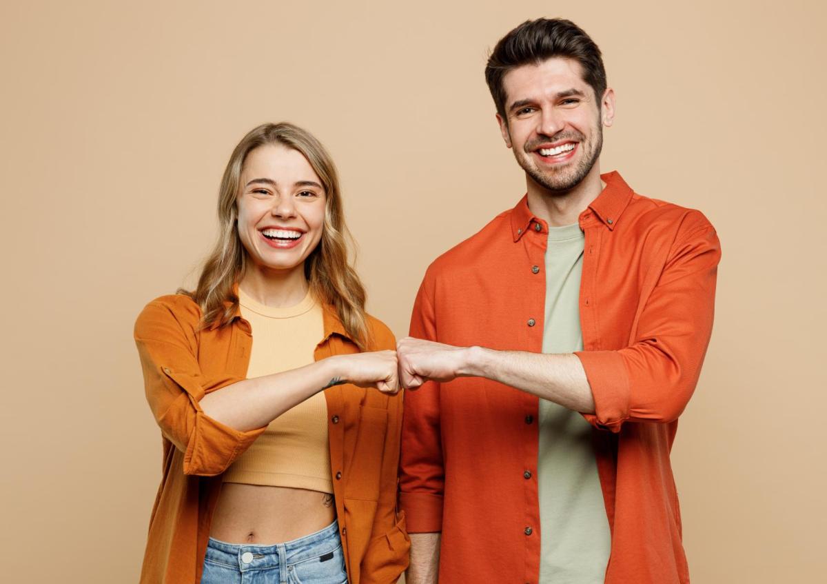 Man en vrouw lachen breed en maken een boksgebaar met hun vuisten naar elkaar toe. Ze kijken vrolijk en tevreden in de camera.