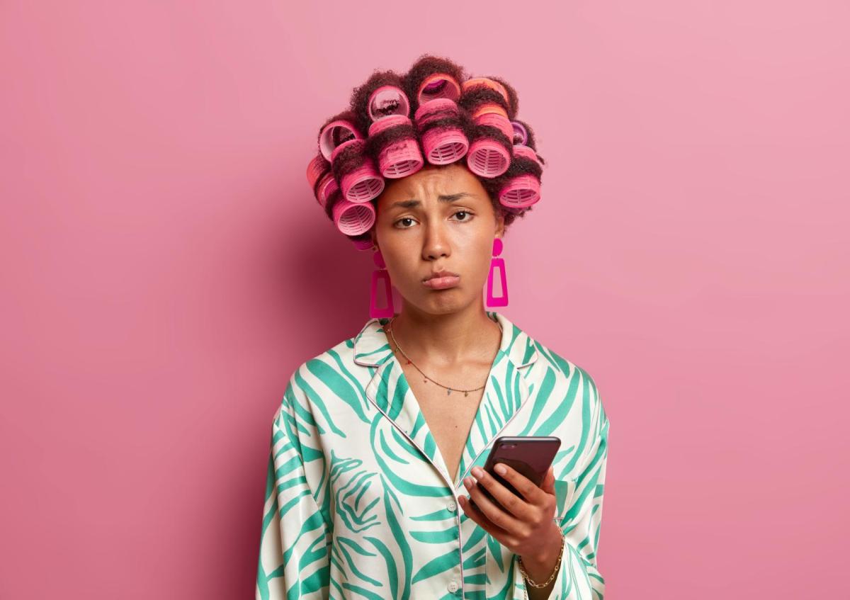 Vrouw kijkt sip en teleurgesteld, met opgetrokken wenkbrauwen en lichtelijk naar beneden getrokken mondhoeken, terwijl ze een telefoon vasthoudt.