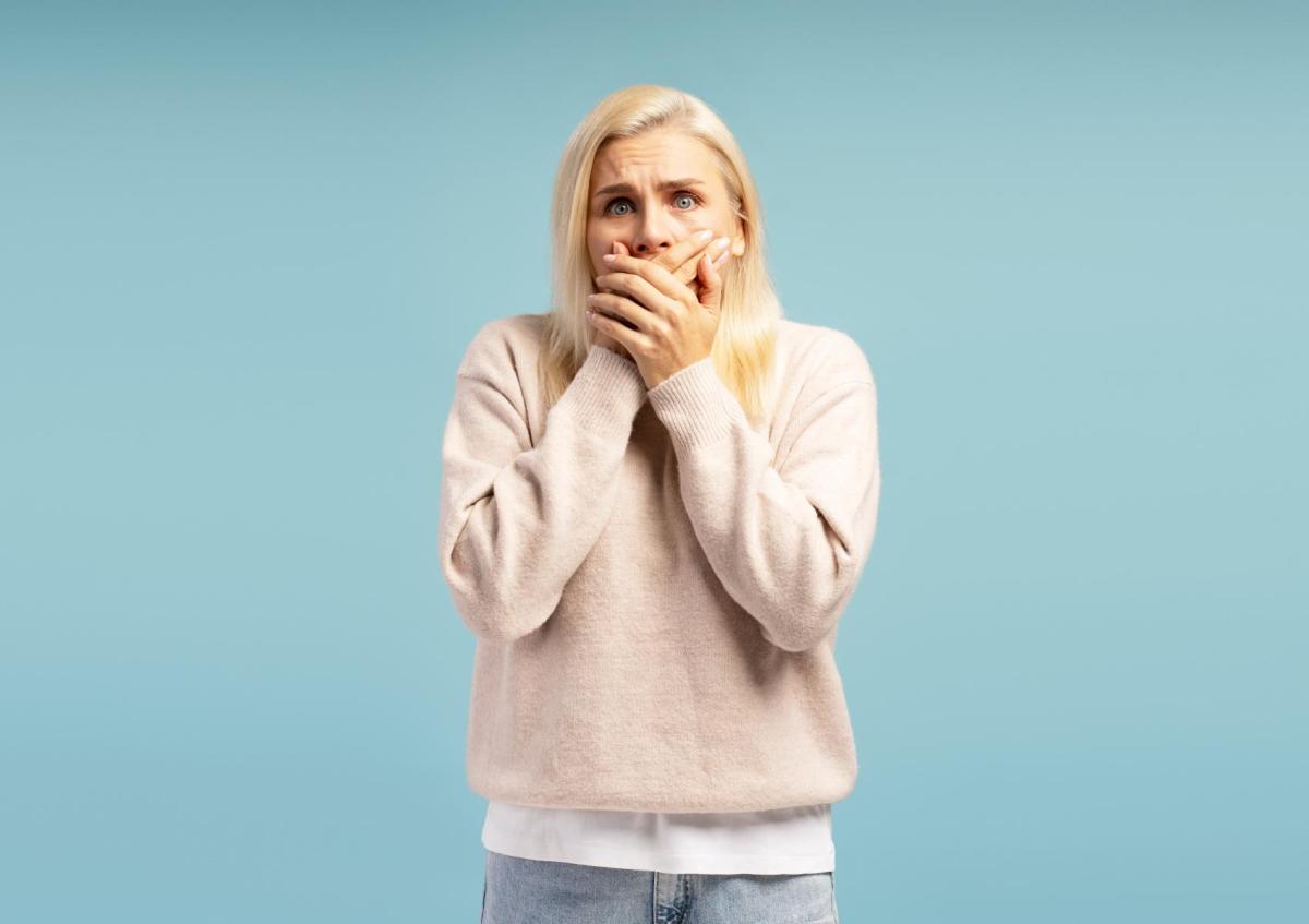 Vrouw bedekt haar mond met beide handen, terwijl ze een geschrokken of bezorgde blik toont