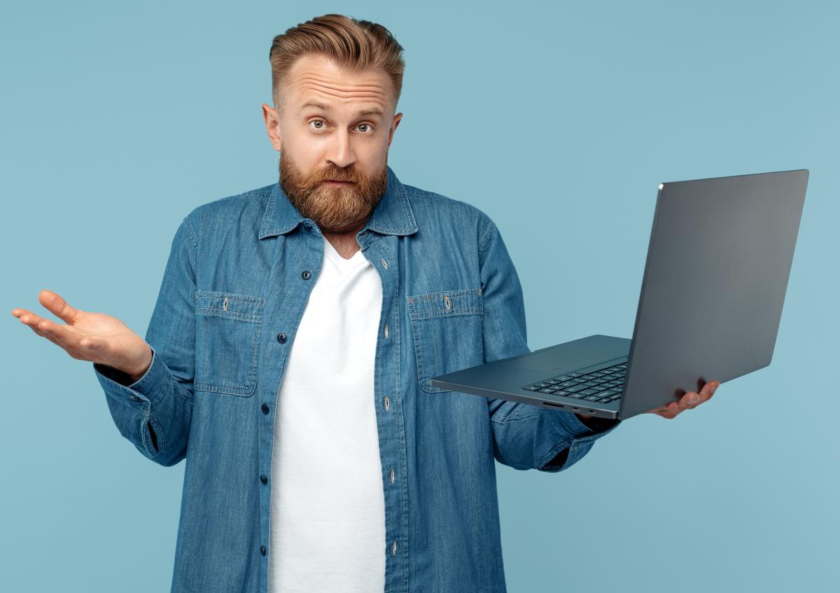 Man met een laptop in zijn linkerhand en haalt zijn schouders op met een onzekere of verwarde blik. 
