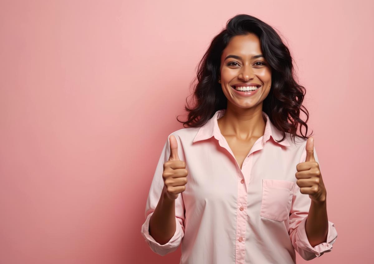 A young woman smiles brightly and gives two thumbs up, expressing approval and positivity.