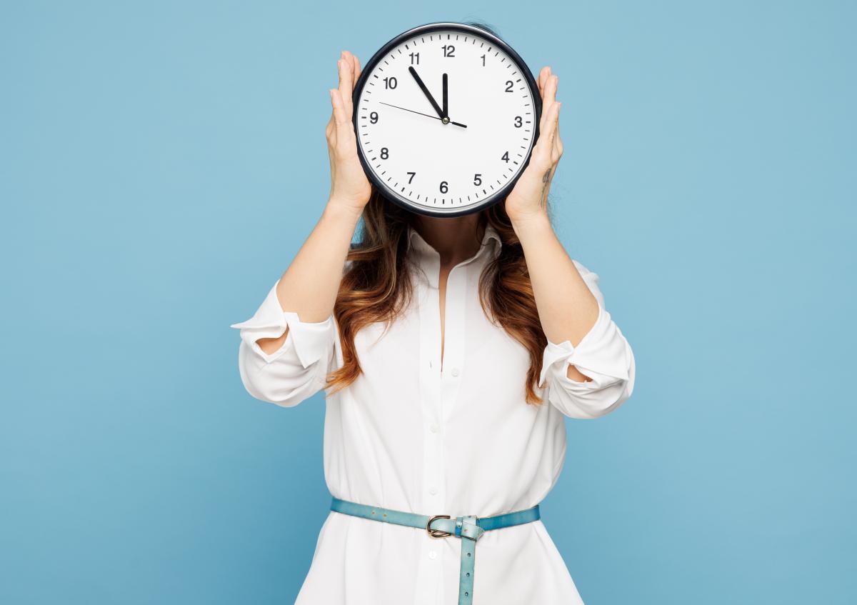 A woman holding a round wall clock in front of her face, covering it completely