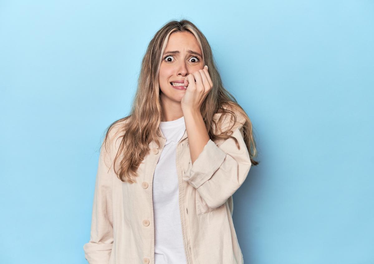 A woman looks worried and anxious, biting her fingernails while gazing slightly to the side.