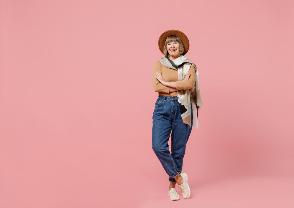 Vrouw staat ontspannen, glimlacht vriendelijk en kijkt recht in de camera. Haar armen zijn gekruist, ze straalt zelfvertrouwen uit.