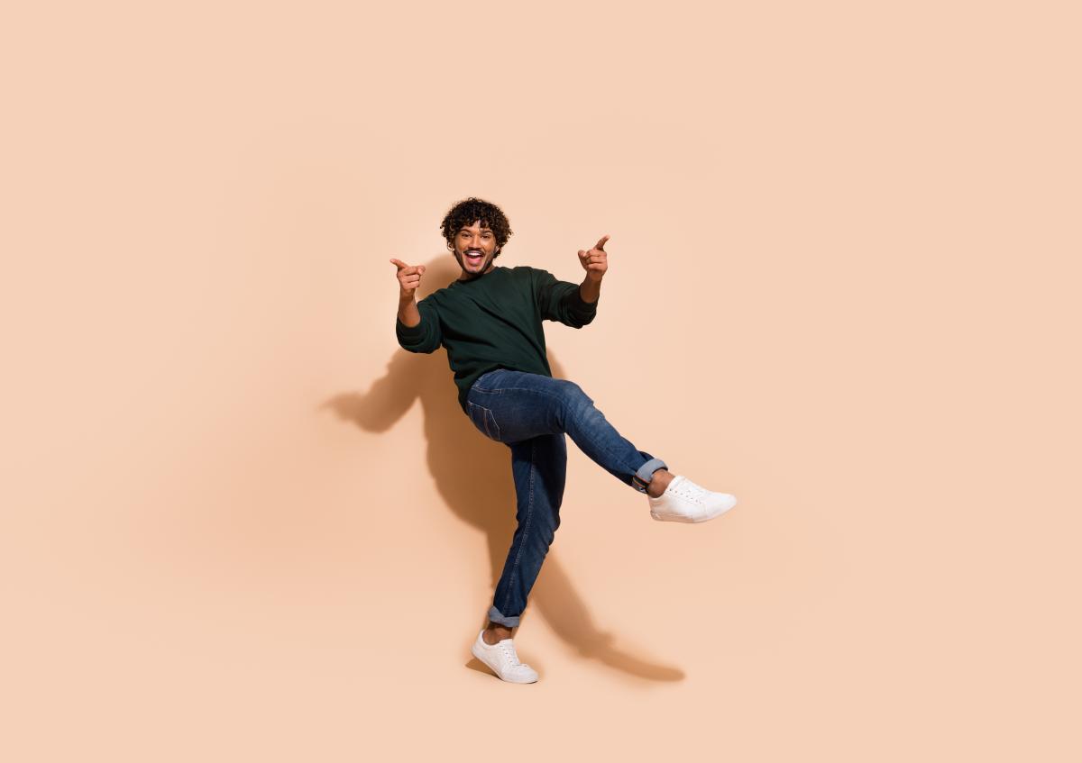A man is playfully posing with one leg lifted and pointing with both hands, expressing excitement and energy