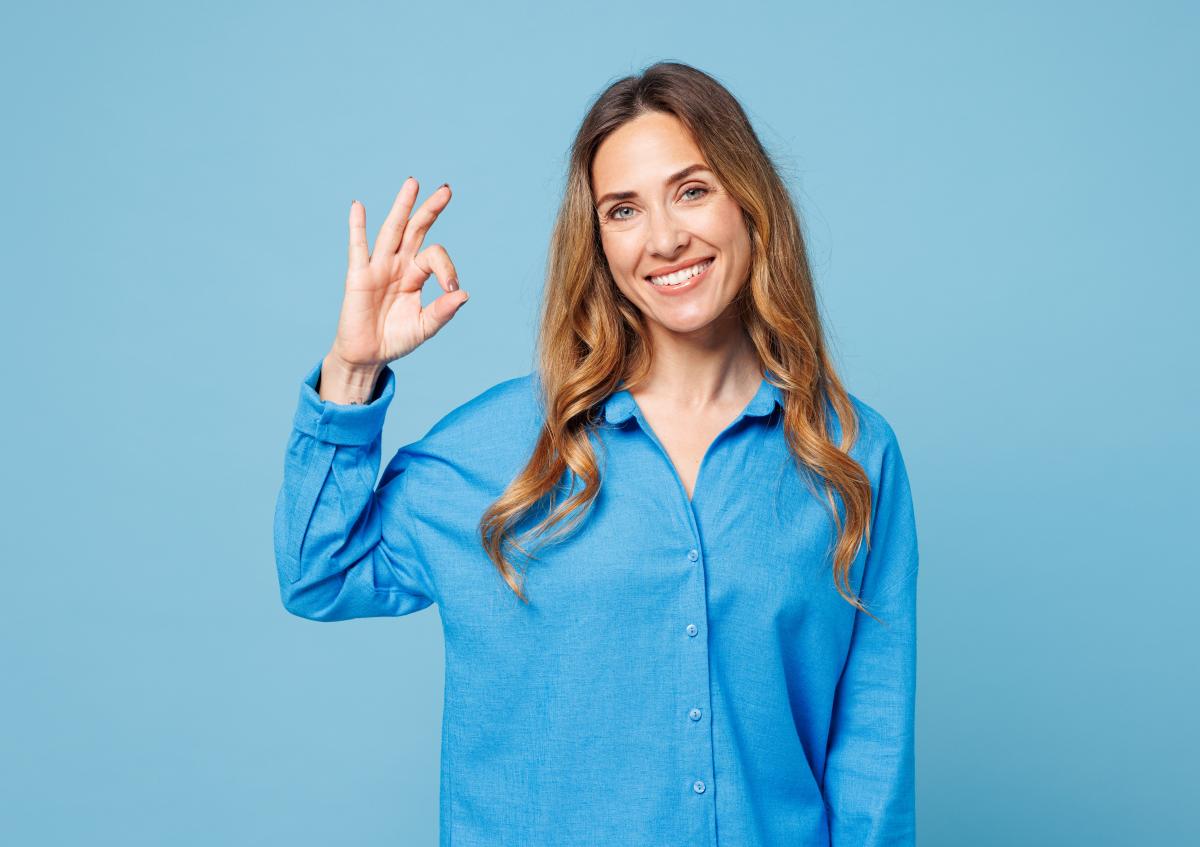 Een vrouw glimlacht vriendelijk en maakt een “OK”-gebaar met haar hand, wat goedkeuring of betekent dat alles in orde is.