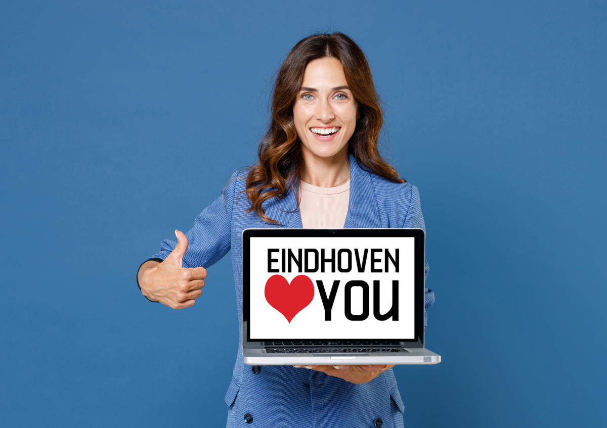 A smiling woman in a blazer holds a laptop showing the message EINDHOVEN LOVES YOU and gives a thumbs-up