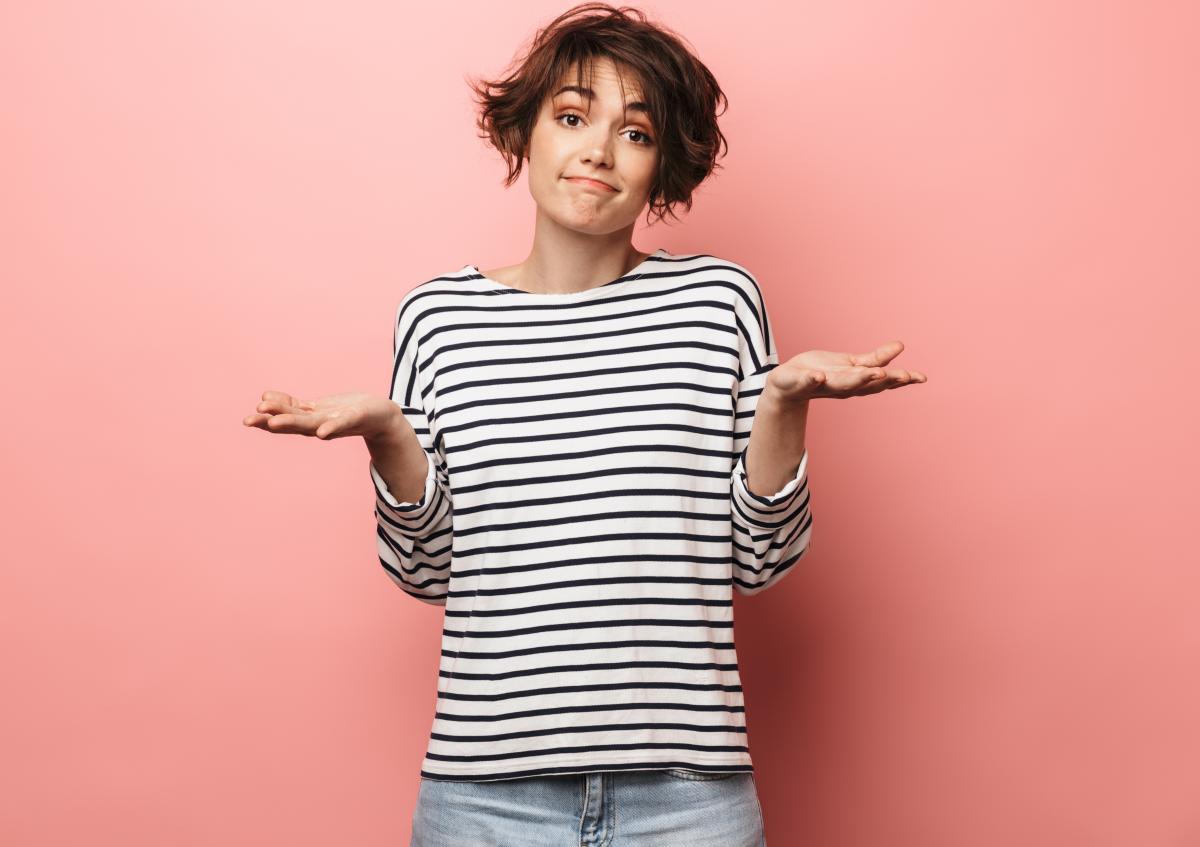 Woman with striped shirt on pink background with palms up, expressing doubt