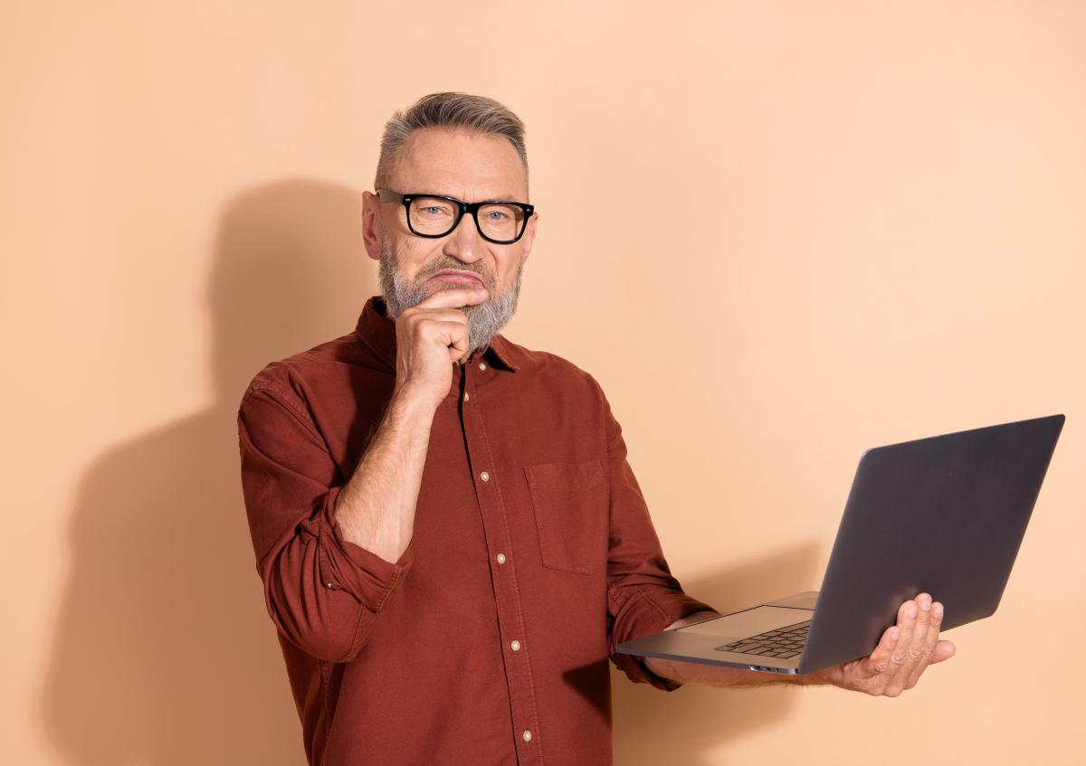 Man in red shirt with laptop is thinking, on light orange, uni background
