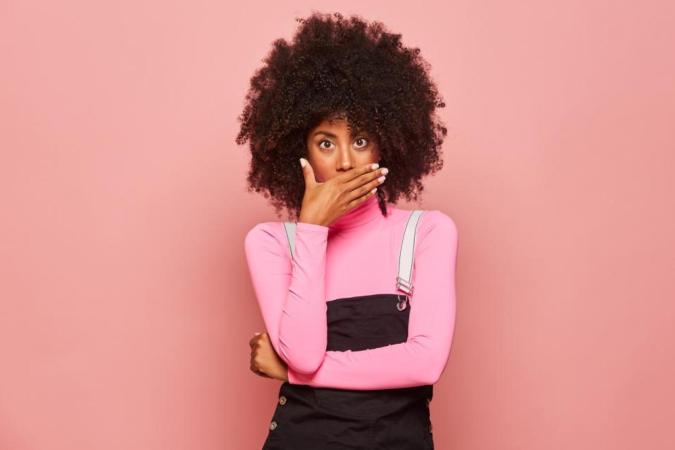 A woman with wide eyes puts her hands over her mouth, expressing shock and surprise