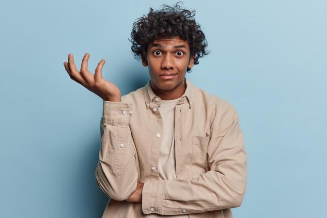 Jonge man kijkt verbaasd en verontwaardigd, met één hand omhoog