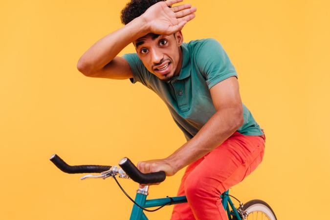 A young man looks anxious or scared, holding the handlebars of his bike tightly with one hand