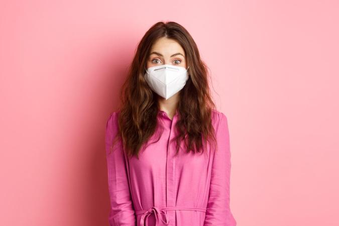 A young woman wearing a protective face mask. Her eyes are wide open, expressing surprise or excitement