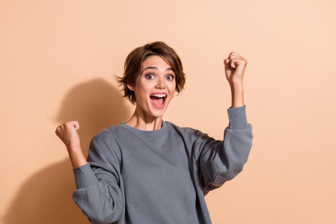 A young woman raising her fists excitedly with a wide open smile, expressing joy or celebration.