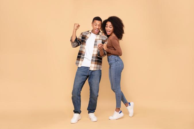 Een gelukkig jong stel kijkt enthousiast naar een telefoon en straalt vreugde en blijdschap uit.