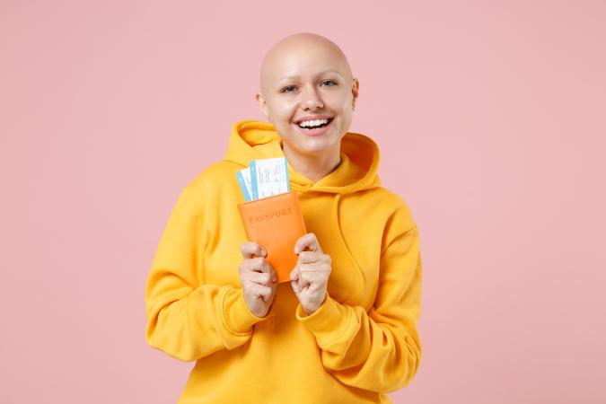 A joyful woman with a shaved head is smiling widely, holding a passport with visible boarding passes