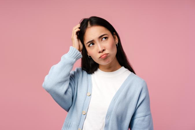 A young woman scratching her head with a puzzled or thoughtful expression, looking slightly to the side.