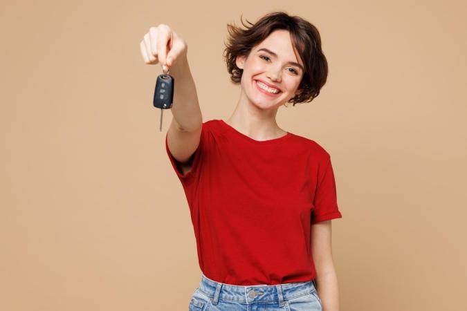 A cheerful young woman holds out a car key towards the camera, smiling broadly.