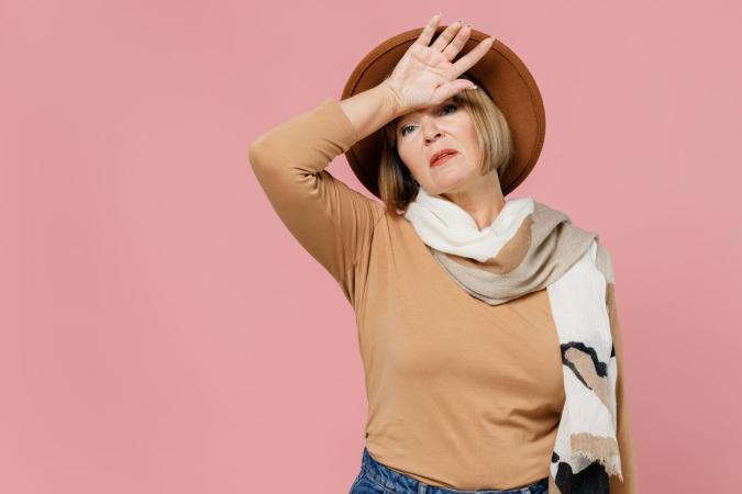 Vrouw kijkt vermoeid of uitgeput omhoog. Ze houdt één hand tegen haar voorhoofd en lijkt even op adem te komen.