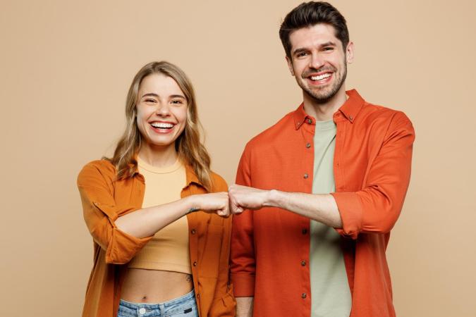 Man en vrouw lachen breed en maken een boksgebaar met hun vuisten naar elkaar toe. Ze kijken vrolijk en tevreden in de camera.