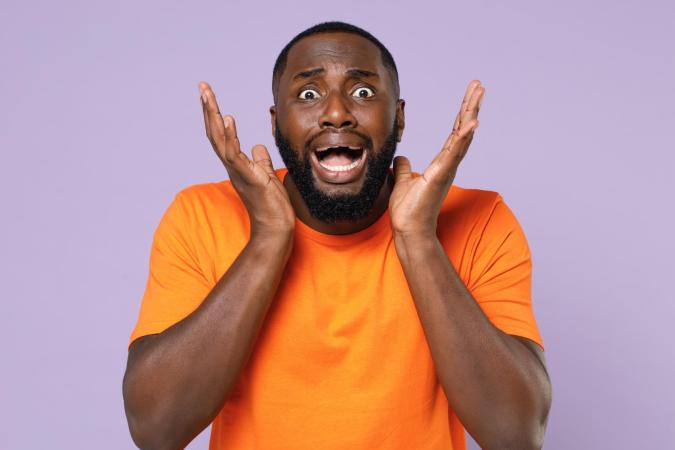 Man kijkt geschrokken en angstig, met zijn mond wijd open en zijn handen naast zijn gezicht.