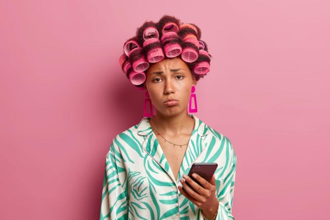 Vrouw kijkt sip en teleurgesteld, met opgetrokken wenkbrauwen en lichtelijk naar beneden getrokken mondhoeken, terwijl ze een telefoon vasthoudt.