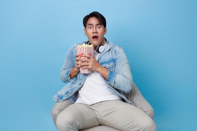 Man kijkt geschrokken en houdt met beide handen een grote bak popcorn vast.