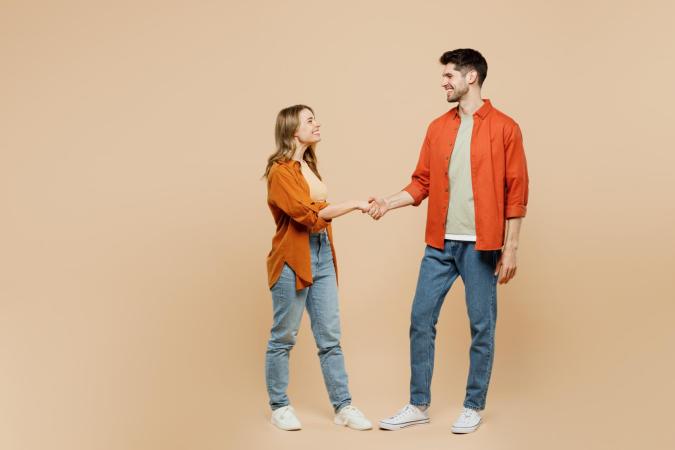 Vrouw en man lachen naar elkaar terwijl ze elkaar de hand schudden, uitstralend dat ze blij en tevreden zijn.