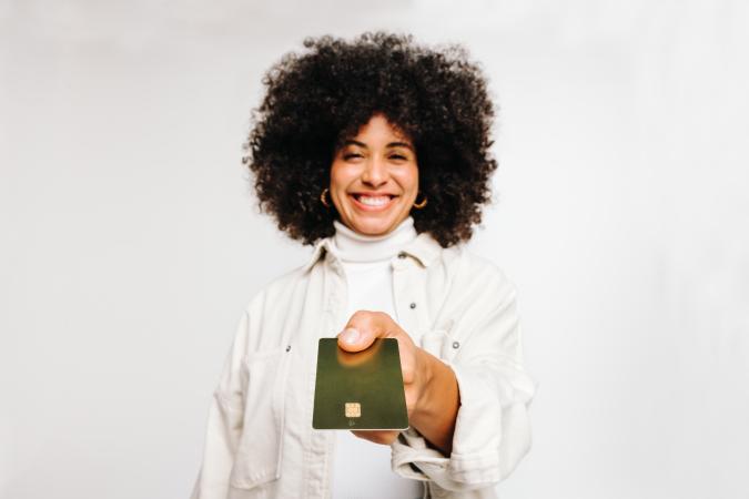 Vrouw lacht breed terwijl ze een pasje (zoals een creditcard of identiteitskaart) naar voren houdt, richting de camera.