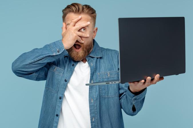 Een jonge man kijkt verward en gefrustreerd, houdt een smartphone in één hand vast en steekt zijn andere hand met gespreide vingers op, alsof hij iets op de telefoon betwijfelt.