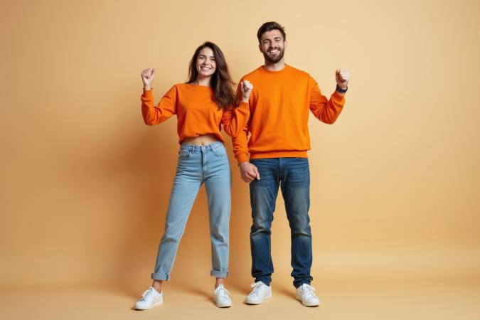 Een jonge vrouw en man staan naast elkaar. Ze glimlachen en maken feestelijke vuisten met gebogen armen, wat blijdschap of succes uitstraalt.