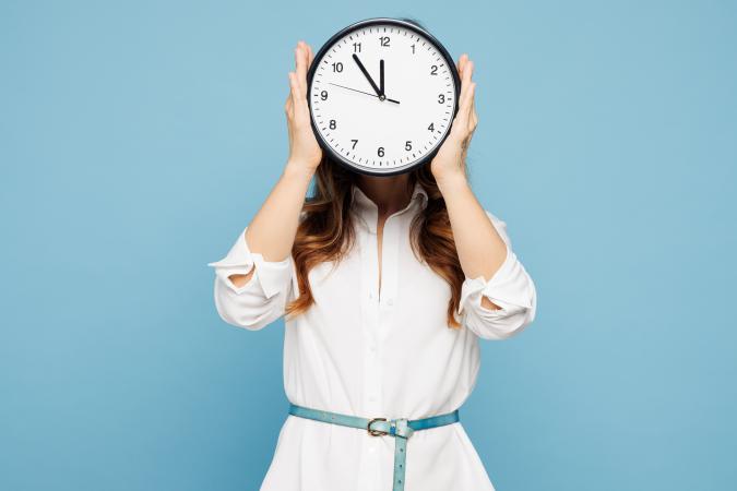 A woman holding a round wall clock in front of her face, covering it completely