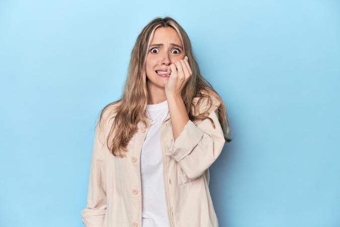 A woman looks worried and anxious, biting her fingernails while gazing slightly to the side.