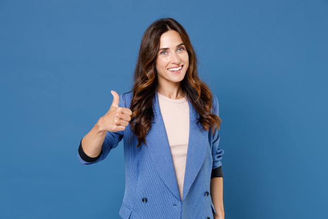 A confident woman smiling warmly, giving a thumbs-up with her right hand, showing approval or encouragement. 