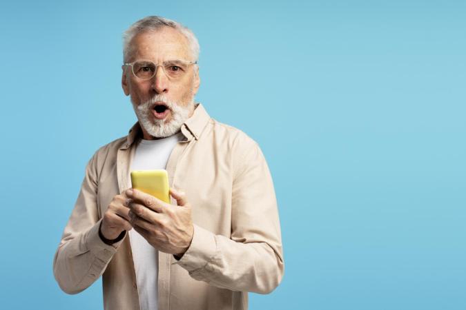 A man holding a mobile phone looks shocked