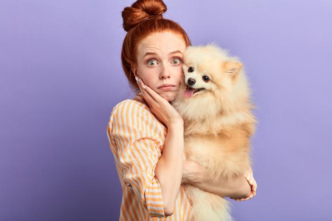Woman in orange and white striped blouse with dog on purple background, afraid of losing her pet