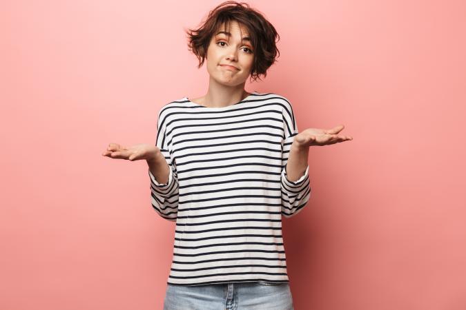 Woman with striped shirt on pink background with palms up, expressing doubt