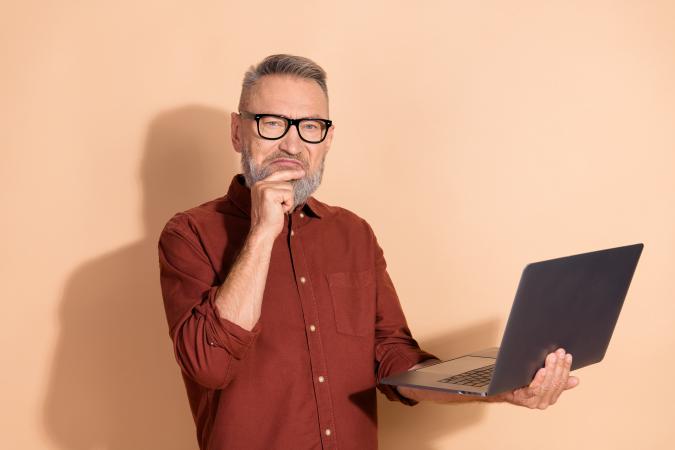 Man in red shirt with laptop is thinking, on light orange, uni background